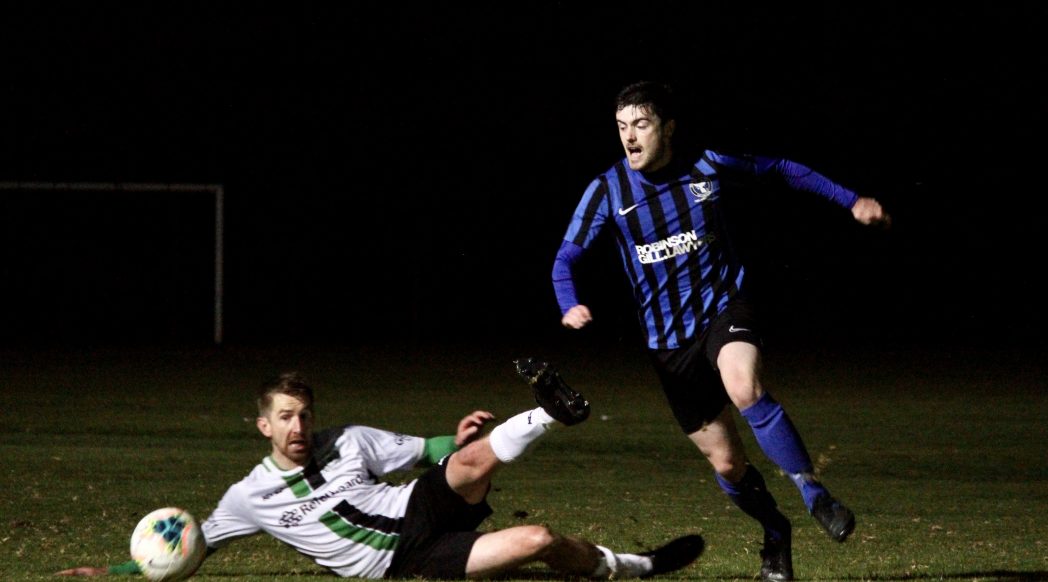 Mitch in a blue and black striped MUSC is on the right side of the photo, running towards a ball in the left bottom corner. An opposition player in a white top is laid on the floor, legs splayed, helpless.