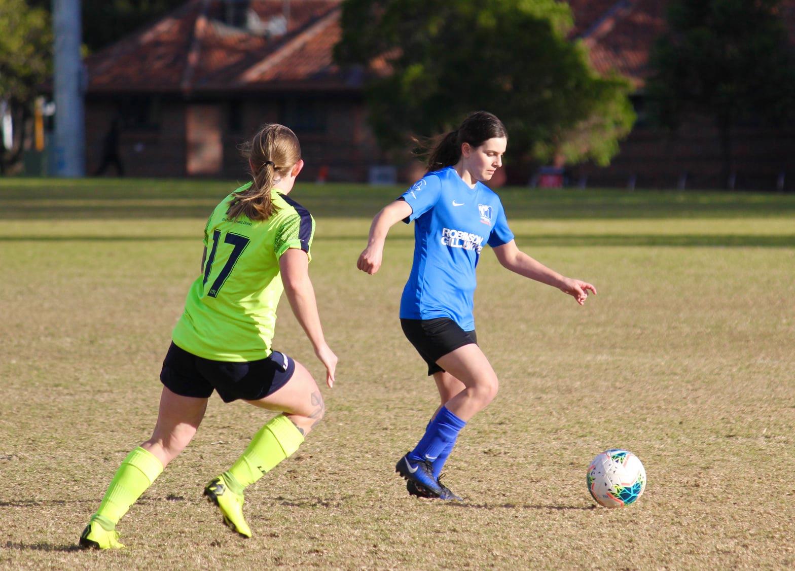 Cicc with the ball at her feet, and an opposition player approaching from the left side of the photo